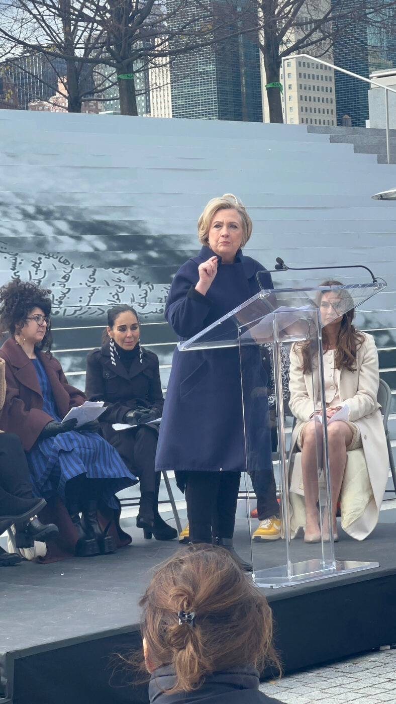 Hillary Clinton speaks at a podium during a women’s rights event in New York City, with two women seated beside her