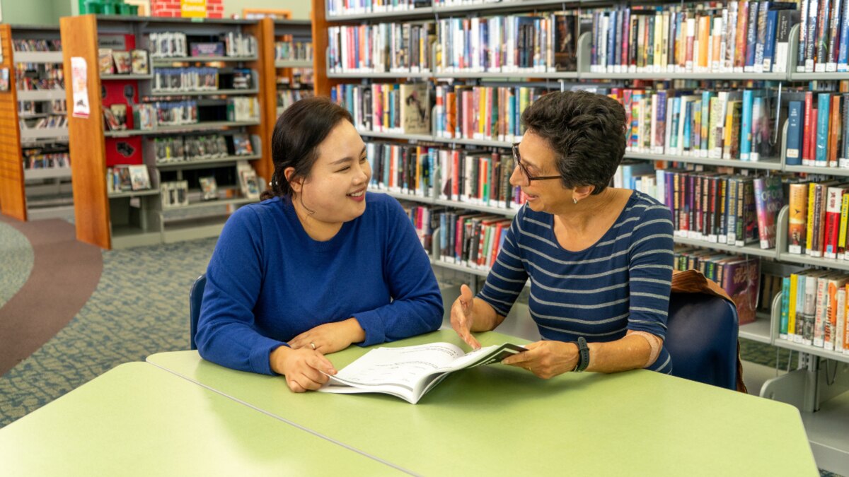 A literacy tutor and learner reading together in a library